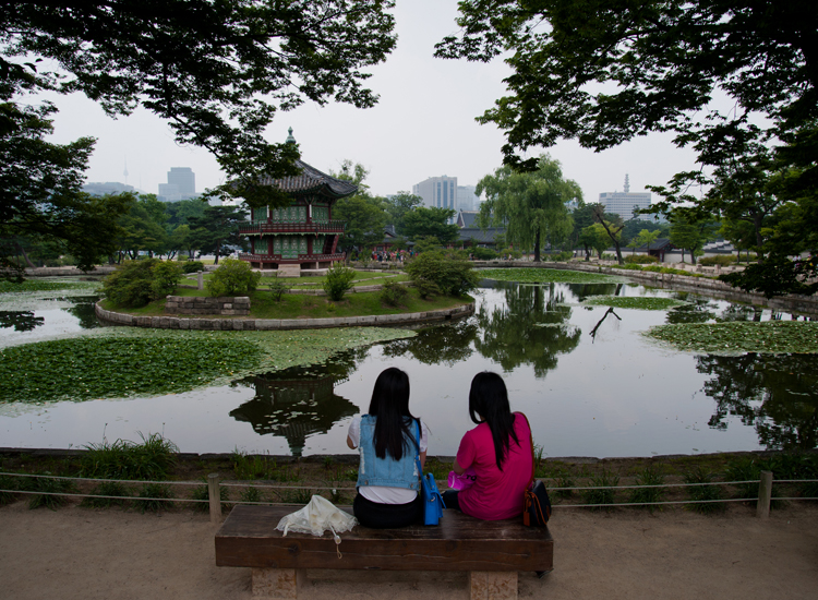due turiste riposano sul bordo del lago che fronteggia Palazzo  Gyeongbokgung